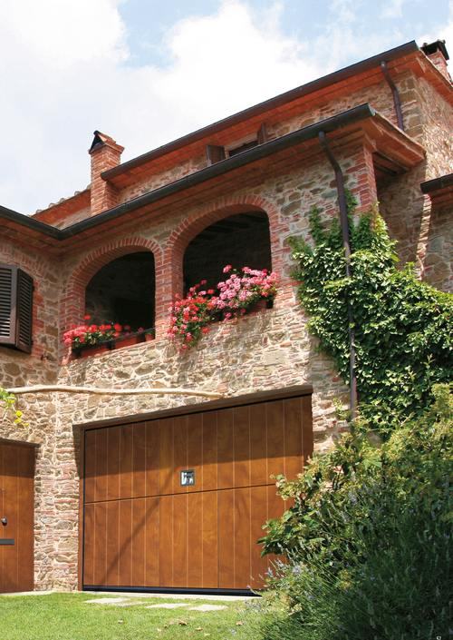 Basculante in legno su una casa rustica in pietra, con porta pedonale coordinata a lato